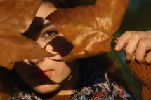 a woman hiding behind fall leaves 