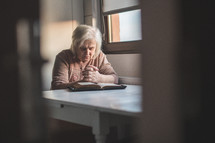 an elderly woman praying over a Bible 