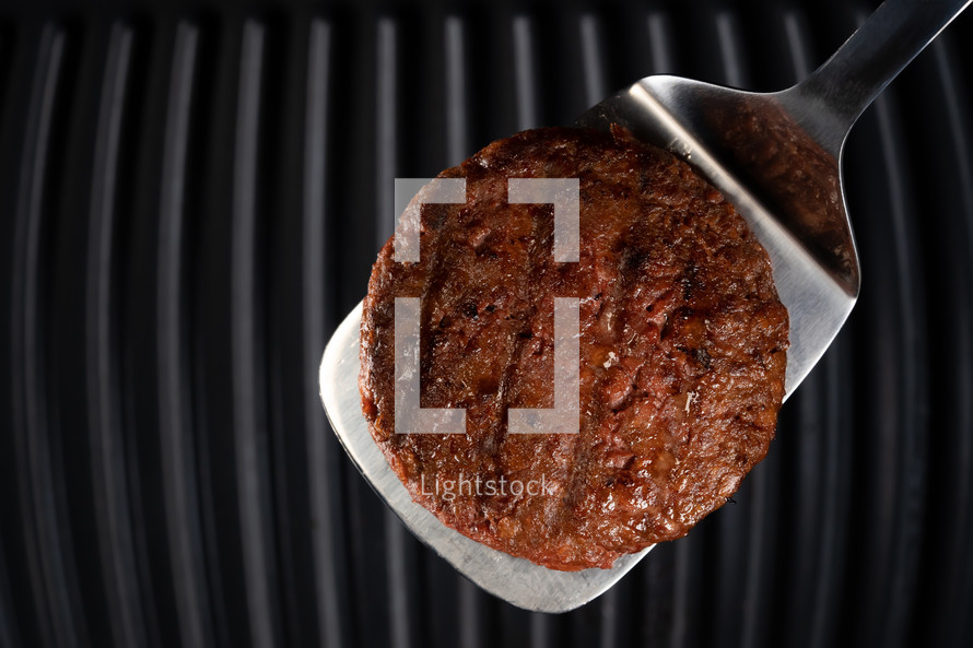 Meat steak on barbecue grilling tool - spatula handle. Cooking beef or pork patty. Raw cutlet for burger. Close-up photo. High quality photo
