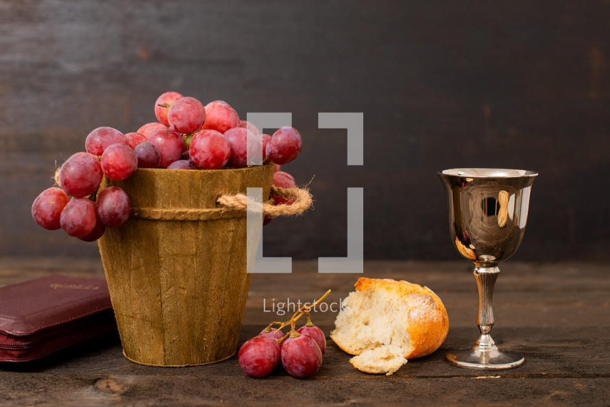 Cup with wine, bread, grapes and bible on wodd table