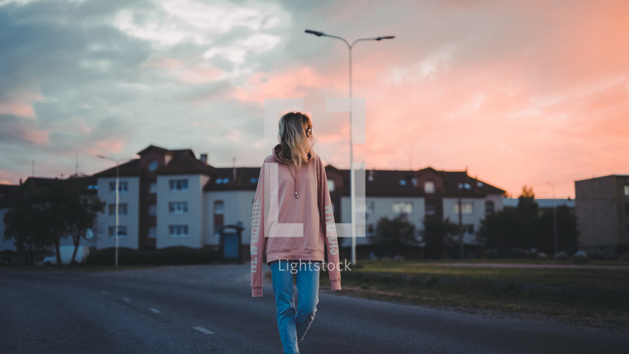 a woman walking down a street at sunset 