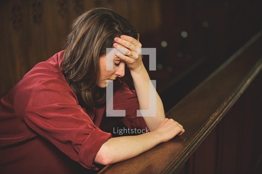 a woman sitting alone in a church pew with her hand on her forehead 