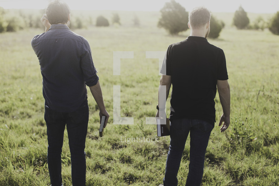 men walking in a field of tall grass holding Bibles 