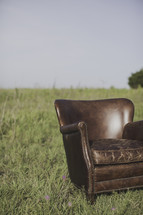 a leather chair alone in a field of tall grass 
