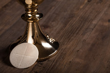 A single communion wafer leaning against a golden goblet.