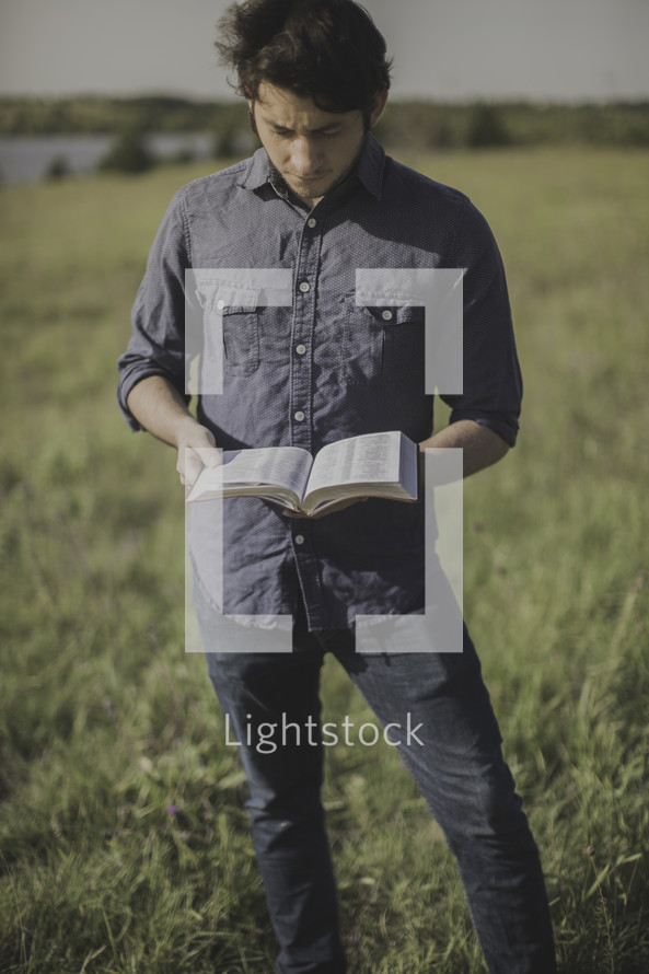 a man standing in a field reading a Bible 