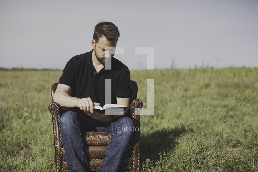 A man sitting in a leather chair reading a Bible 