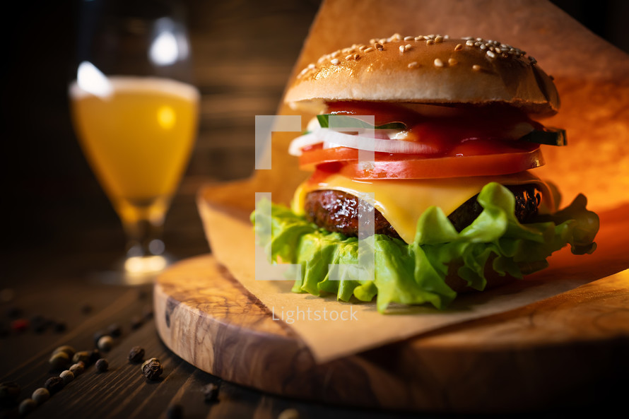 Big homemade burger on wooden stand. Glass with light beer. Beautiful restaurant composition demonstrating juicy appetizing fast food. High quality photo