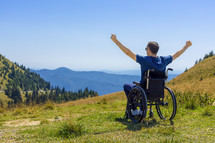 Young man in a wheelchair enjoying fresh air in a sunny day on the mountain
