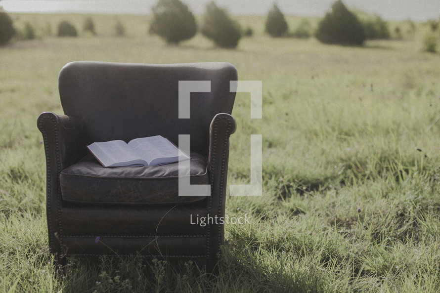 an open Bible in a leather chair in a field 