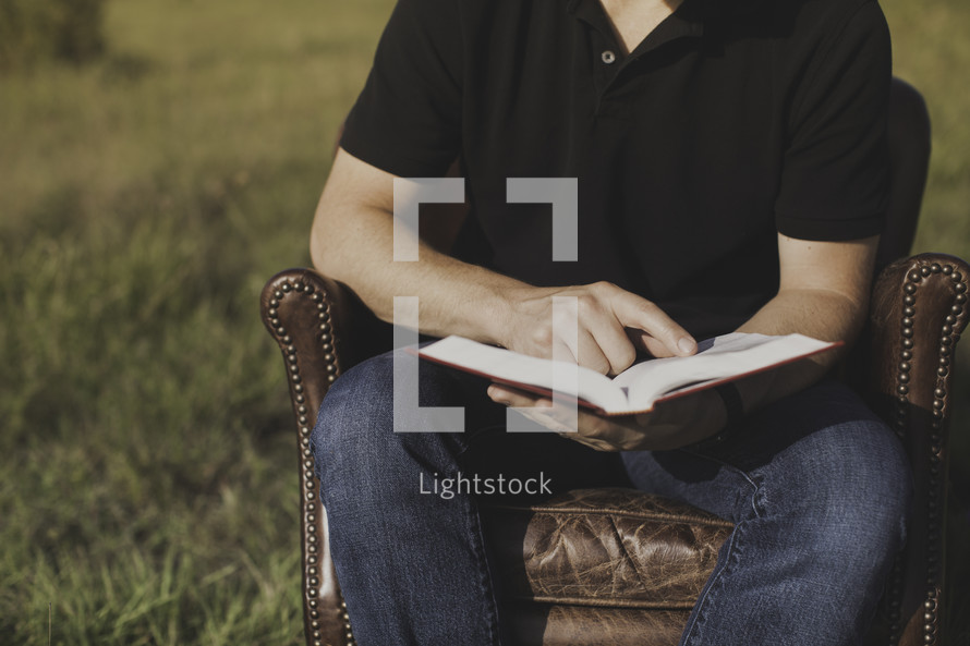 a man sitting in a leather chair reading a Bible 