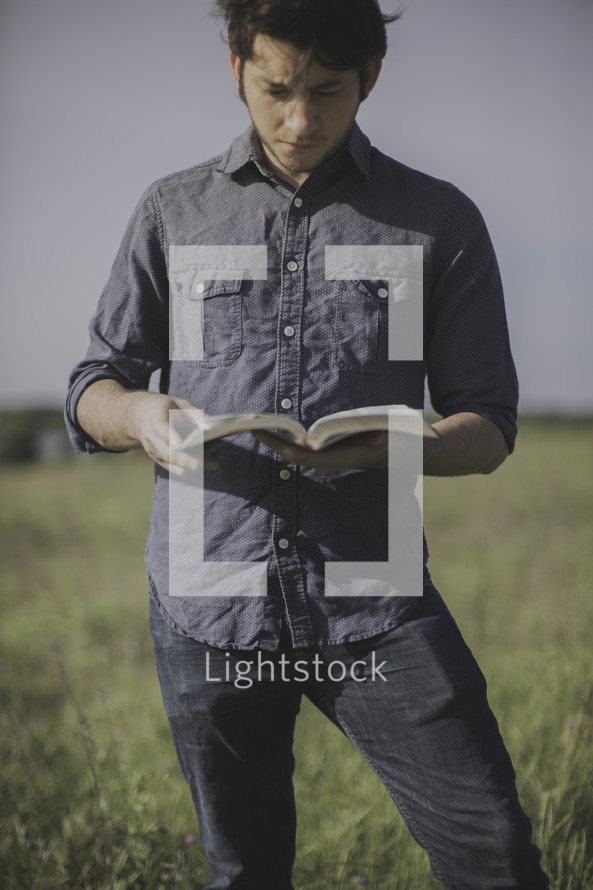 a man standing in a field of tall grass reading a Bible 