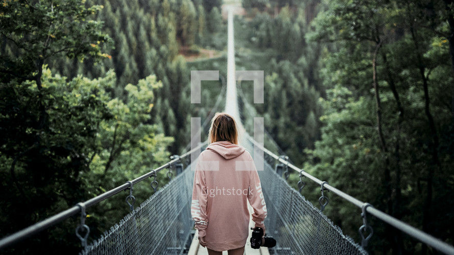 a woman with a camera crossing a swinging bridge 