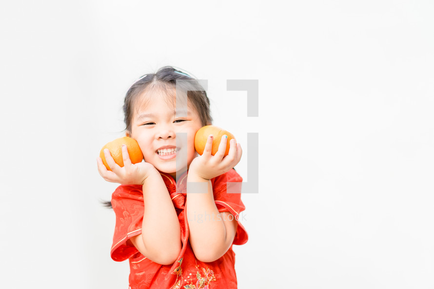 a little girl in traditional Chinese dress holding oranges 