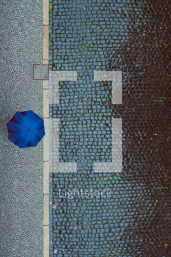 overhead view of a blue umbrella and cobblestone street