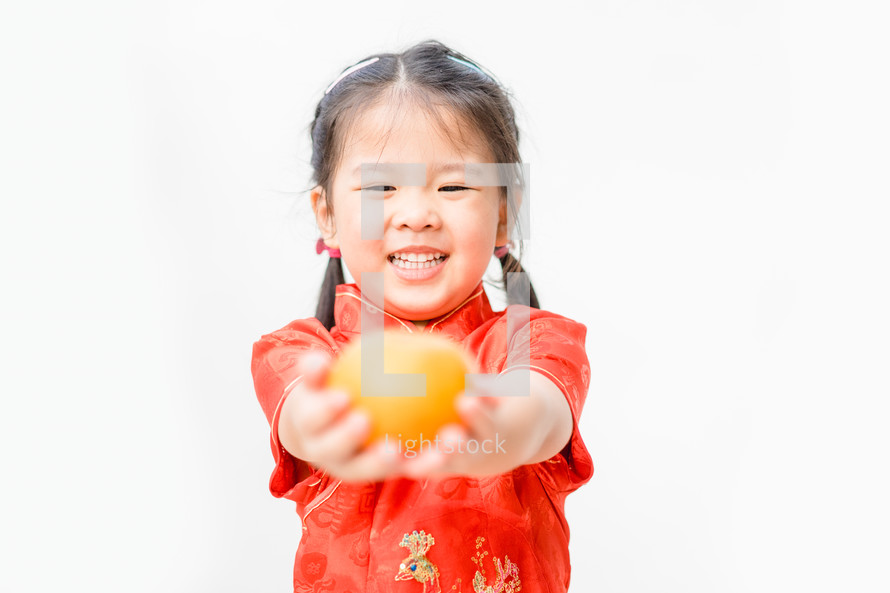 a little girl holding an orange dressed in traditional Chinese dress 