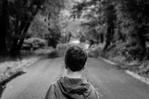 a young boy standing alone on a rural road 
