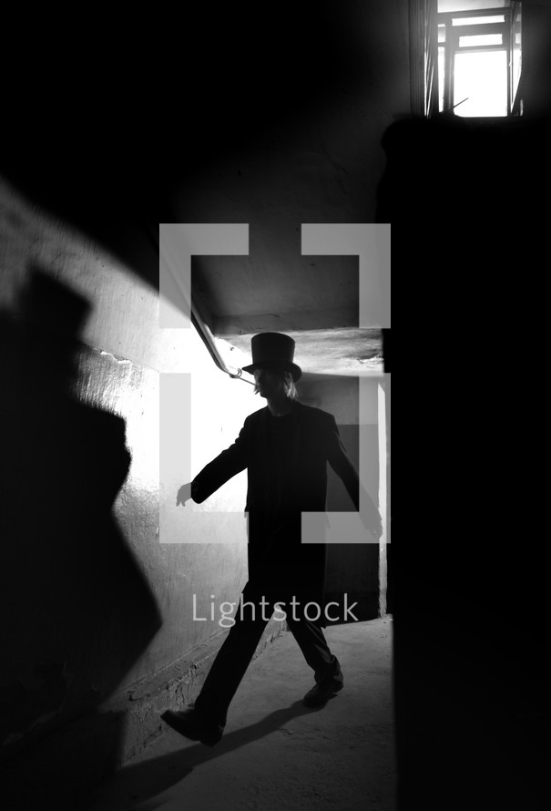 a man in a top hat walking in the shadows 