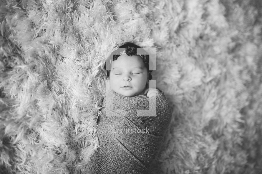 swaddled baby on a fur rug 