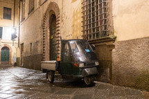 three wheeled vehicle parked on a cobblestone street 