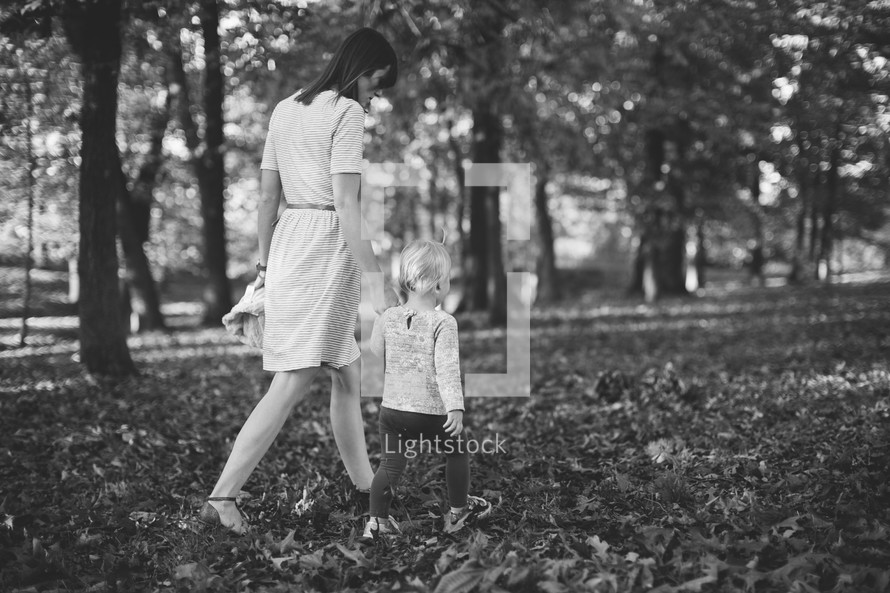 a mother and toddler daughter walking through fall leaves 