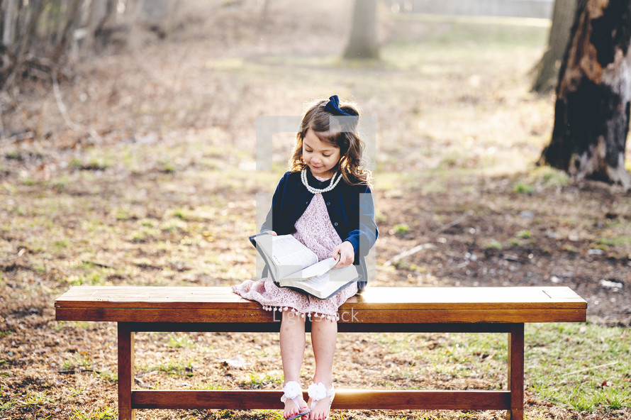 a little girl sitting on a bench reading a Bible 