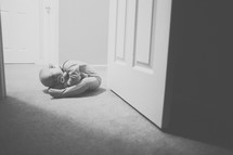 A baby lays on the floor in a doorway.