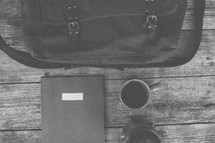 A bag, notebook, coffee mug and french press on wood