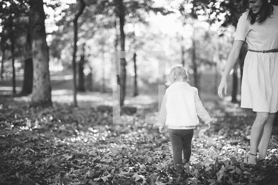 a mother and toddler walking through fall leaves 