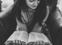 A young woman siting in a chair reading the Bible