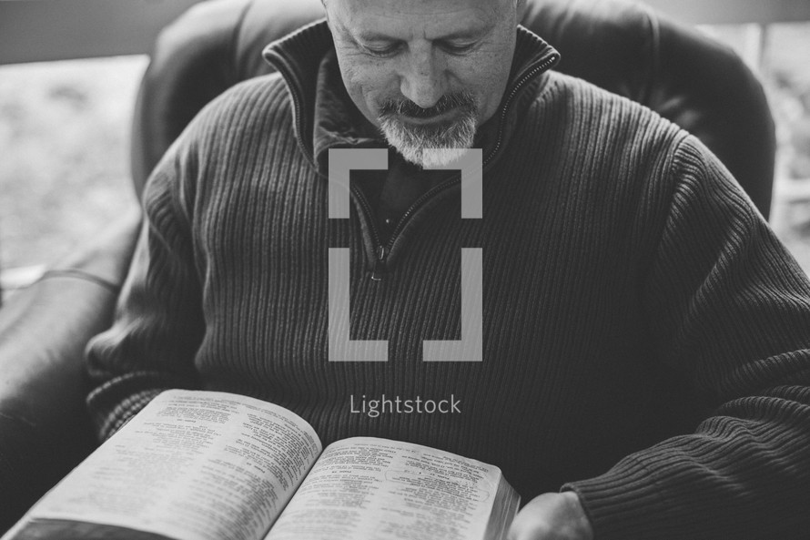 A man reading a Bible sitting in a chair 