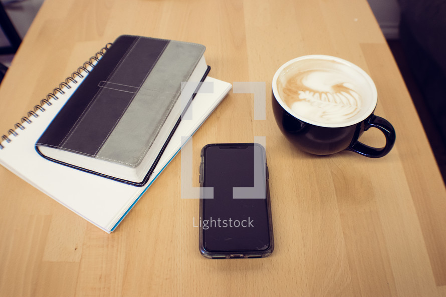 Bible, notebook, cellphone, and coffee cup on a wood table 