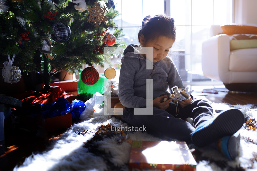 child playing with toys under a Christmas tree 