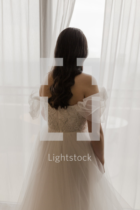Back view of a bride looking out a window on her wedding day.