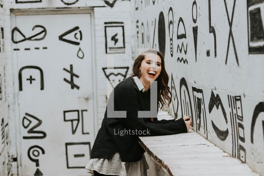 smiling woman posing in front of black and white street art 