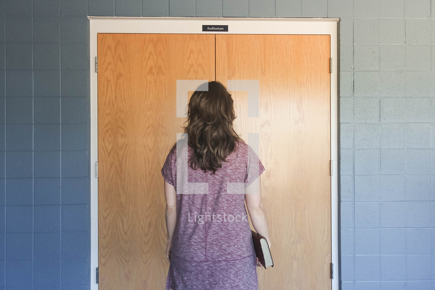 a woman holding a Bible entering through church doors 