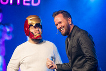 a minister on stage with a man dressed as a super hero 