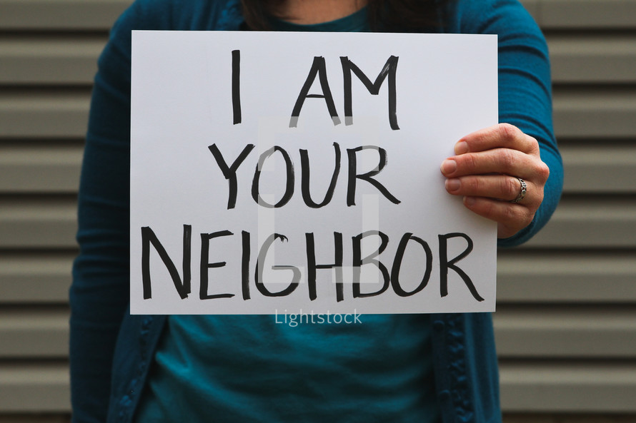 A woman holding a sign that says I am your neighbor