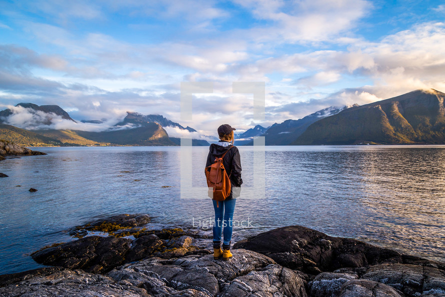 woman standing on rocks near a lake shore looking out a mountains