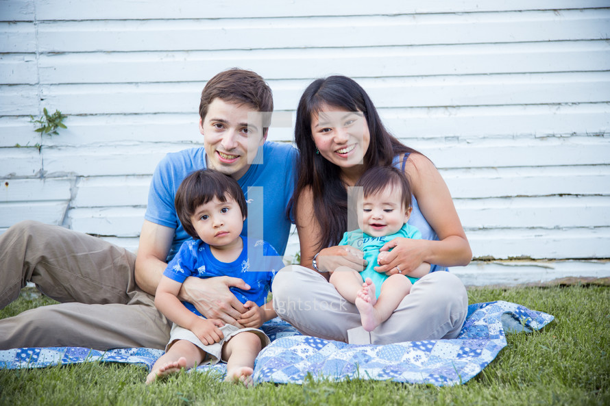a family sitting on a blanket in the grass 