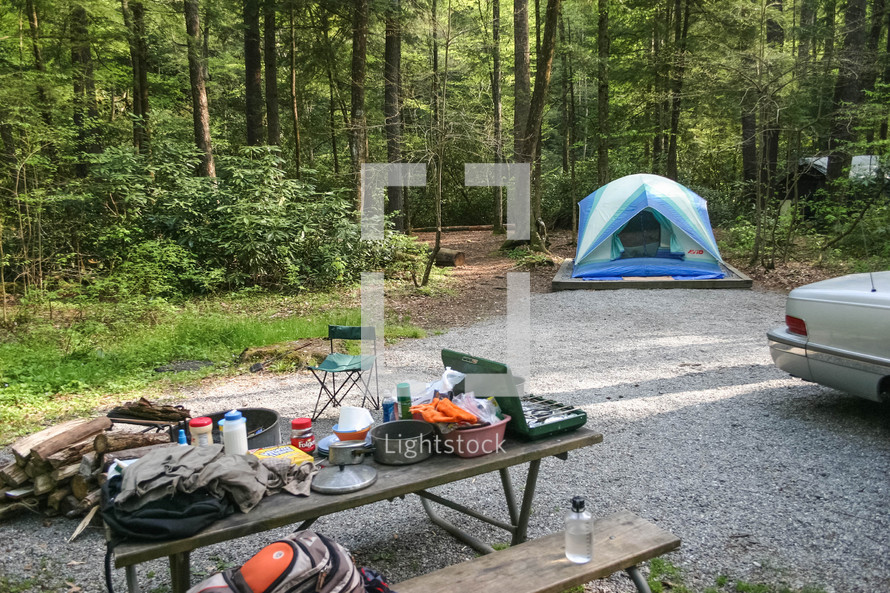 camping gear on a picnic table and tent at a campsite 
