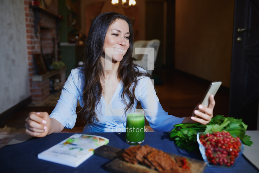 Woman at the table with healthy food making mobile photo selfie for her Internet blog