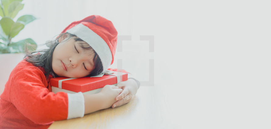 a little girl in a Santa suit sleeping on a Christmas gift 