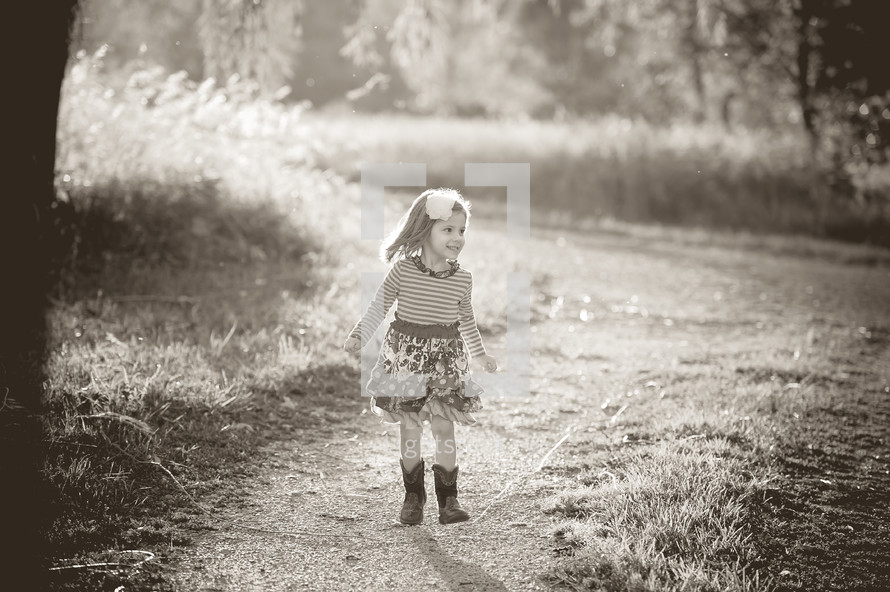 A little girl in a dress and cowboy boots outdoors. 