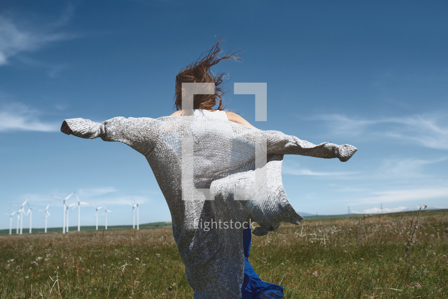 woman running in field in front of a wind farm 