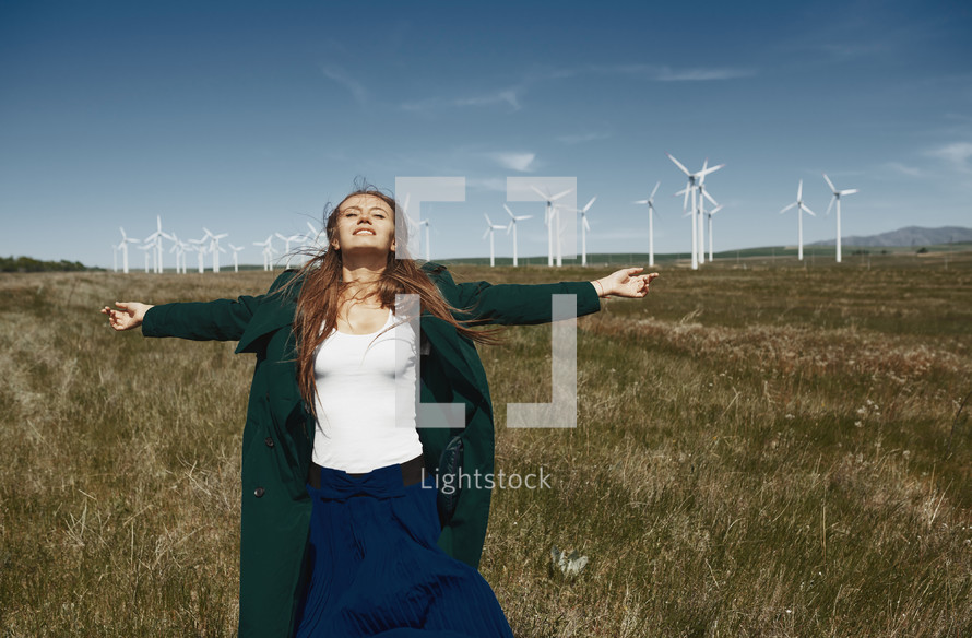 a woman with outstretched arms standing in front of a wind farm 