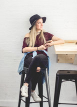 young woman sitting on a stool holding a cellphone 