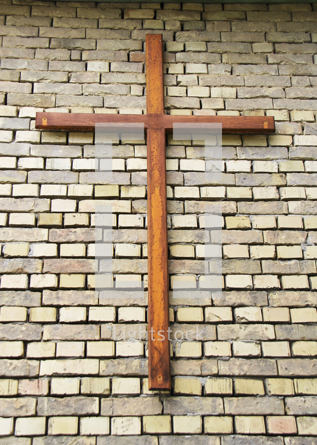 wooden cross hung on brick wall 