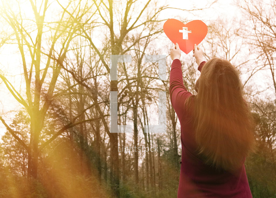 a woman holding up a heart with a cross 