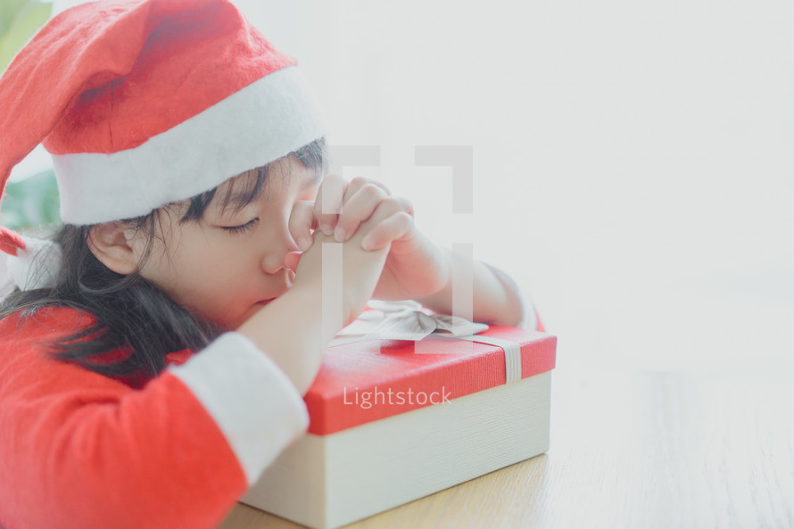 a little girl in a Santa suit praying over a Christmas gift 